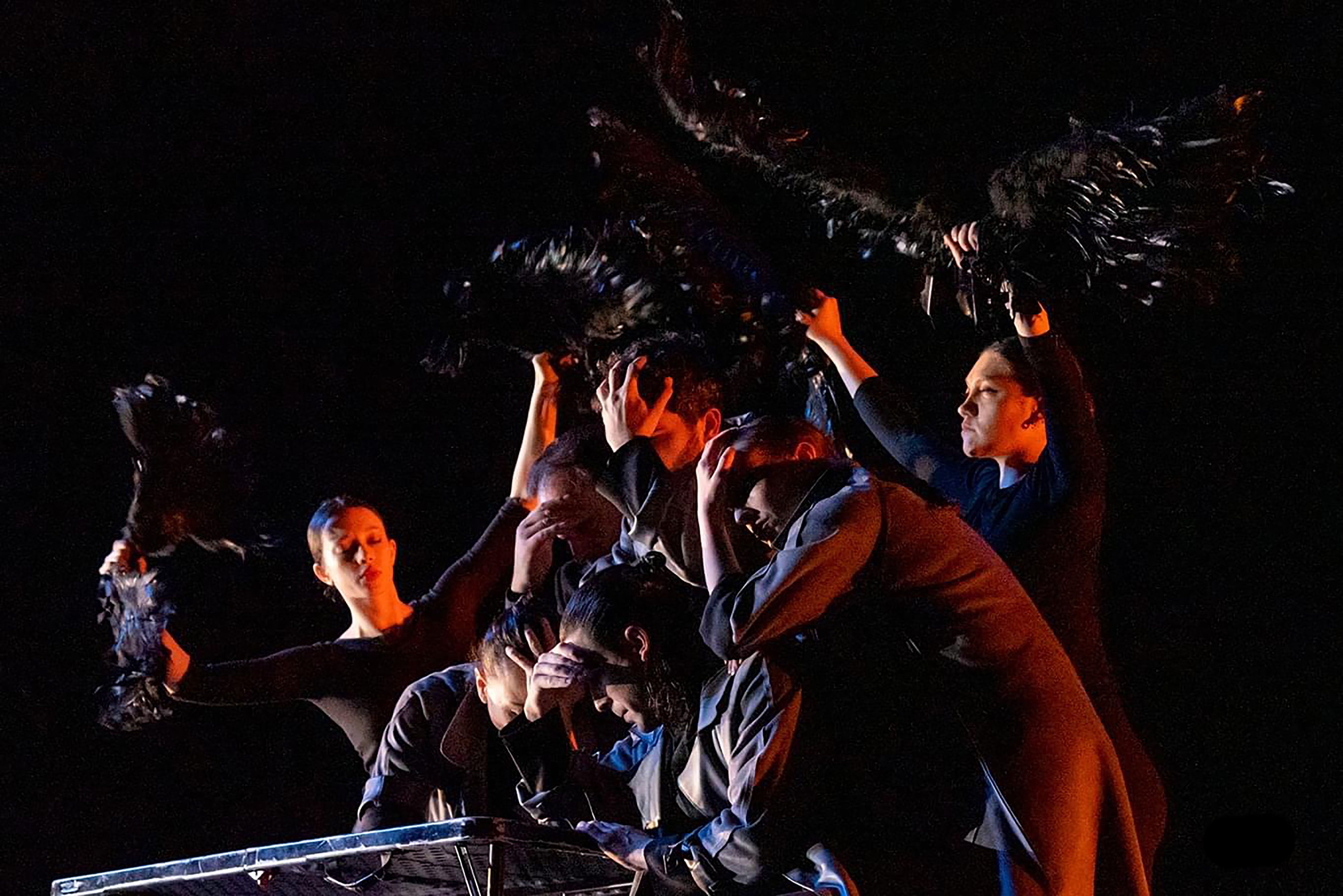 A dark scene featuring a tableaux that inclues black costumed dancers holding feathered fans that resemble night creatures