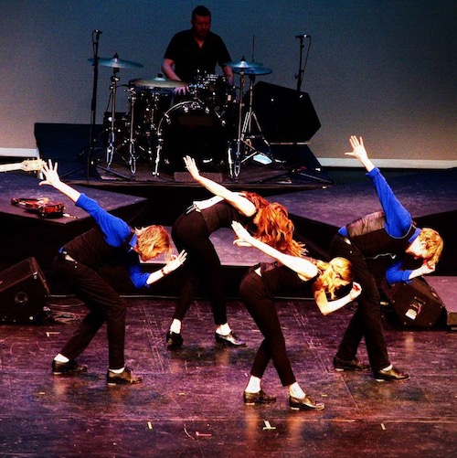 Four dancers bend at the waist. Their right arm extends straight behind them while their left is placed near their face.