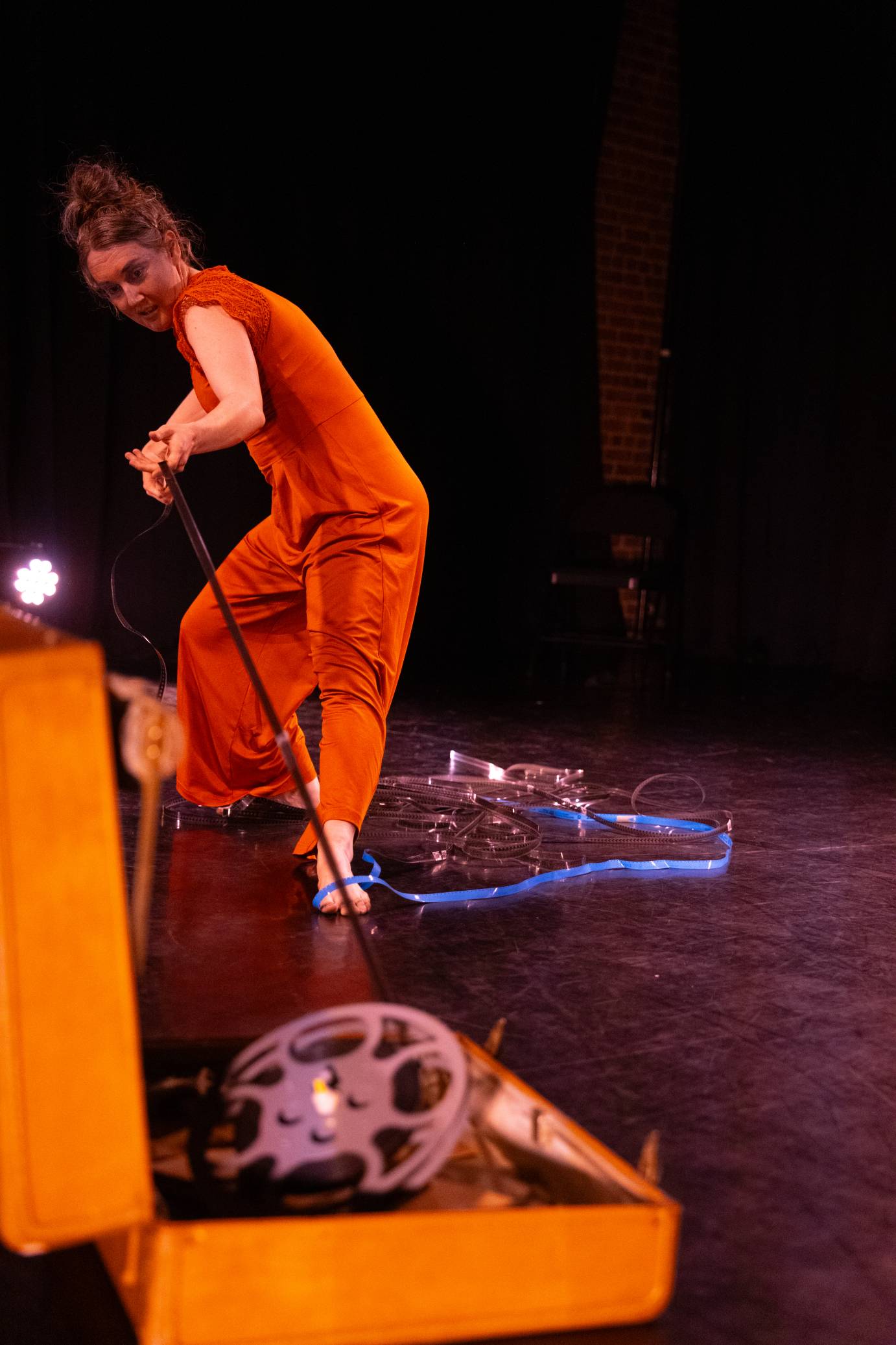 A woman in an orange jumpsuit leans forward as she pulls on reel-to-reel tape.