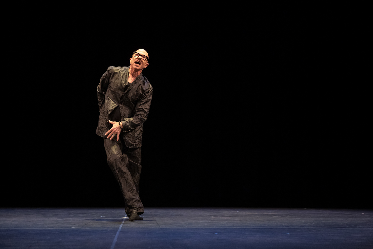 With mouth open, the choreographer dressed in baggy black pants and jacket, spirals and dips to the left