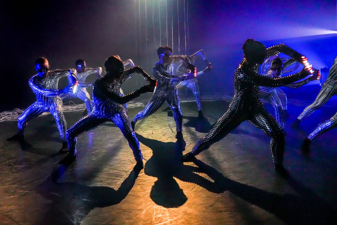 a chorus of dancers in silver thorny costumes and glasses hold their cell phones 