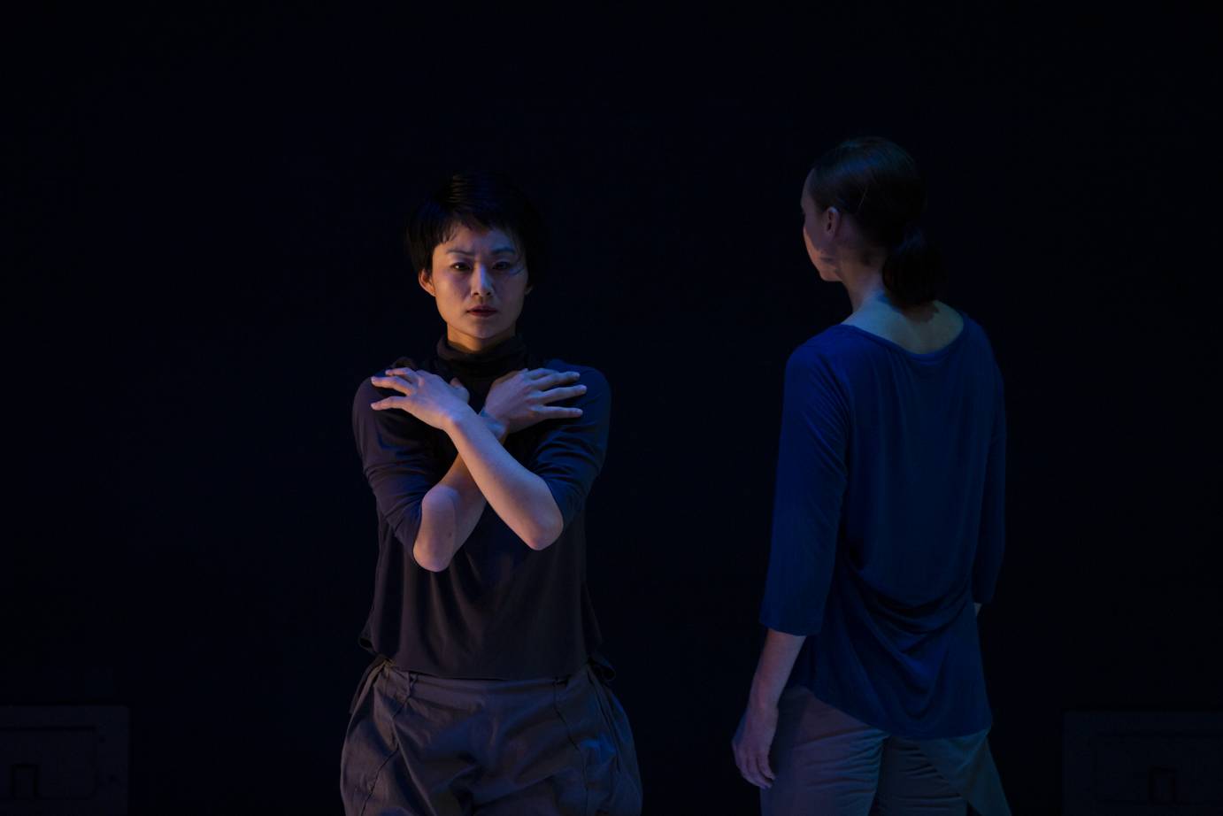 A woman stares straight ahead, her arms crossed over her chest