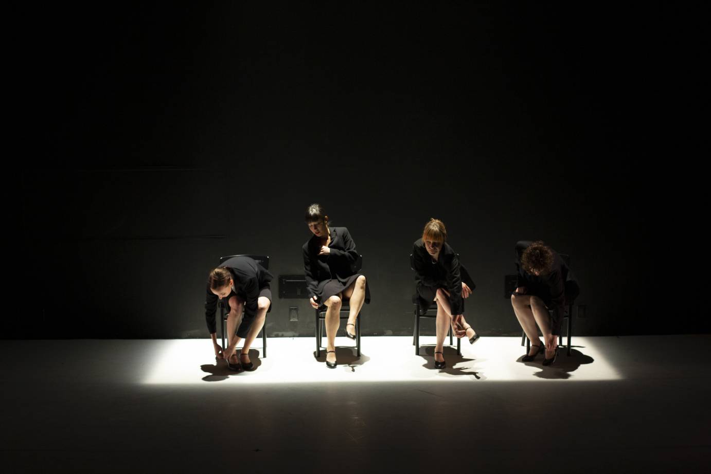 Four businesswomen sit in chairs taking off their high heels