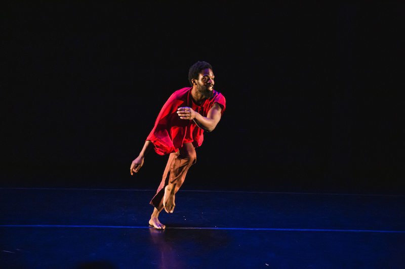 In a red shirt and brown pants, Kyle Marshall swings one arm in front of his body while one leg lifts at the knee
