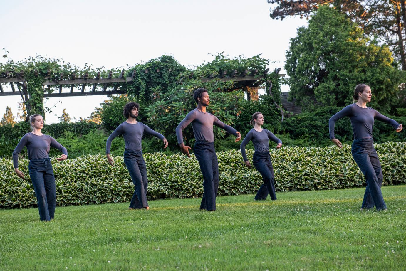 Dancers stand with bent knees with their rounded, one in front of their stomach, the other behind them