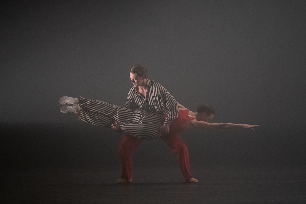 in a cloudy atmosphere a man in a black and white striped shirt, red pants white sneakers, has caught a woman in black and white striped pants, a red tank and white sneakers. She looks as if she has dived into him and is lucky to have been caught