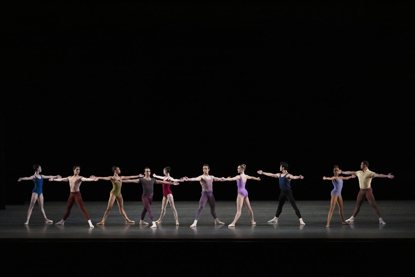 NYC Ballet Dancers in a line, wearing colorful leotards and tights, and standing in wide second postions or wide fourth positinos 