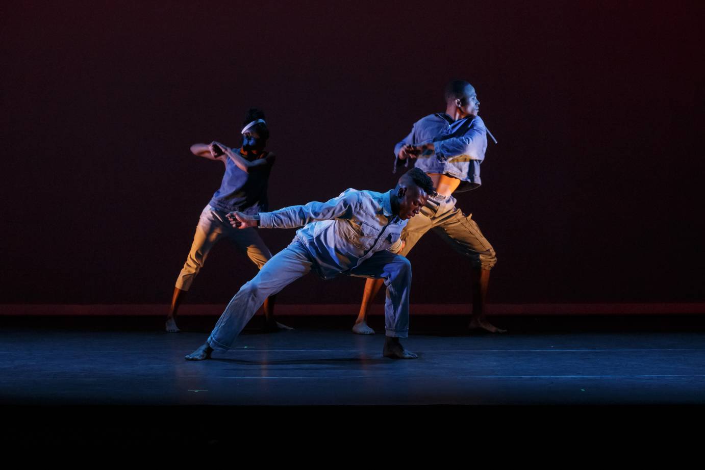 Three dancers on different levels and facings lunge forward.