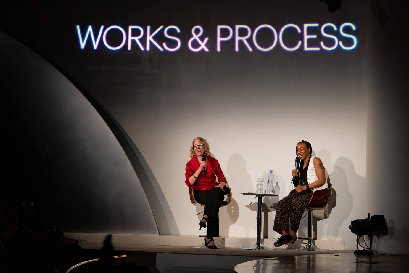 Two seated women holding microphones smile to the audience.
